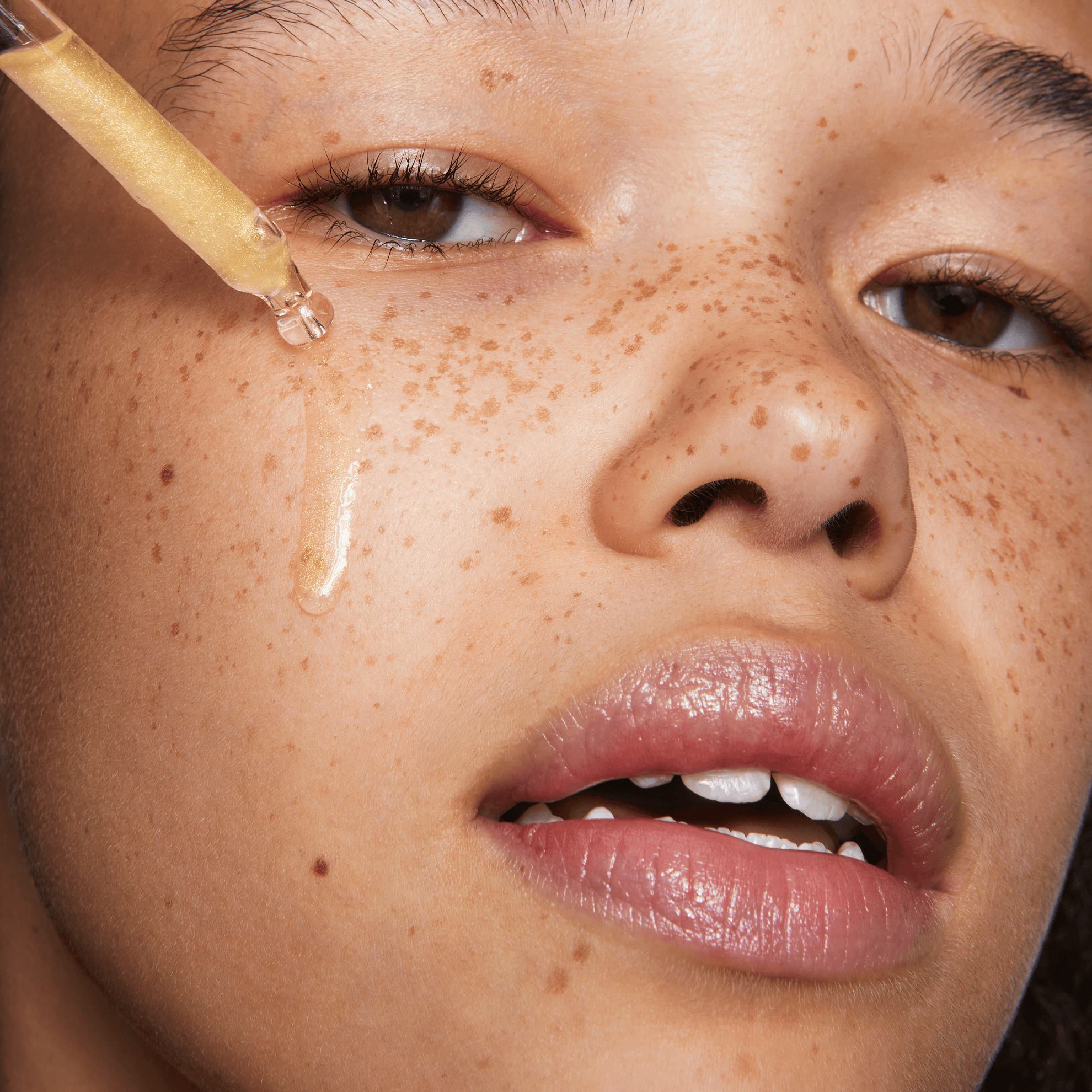 a woman applying a drop of liquid on her face