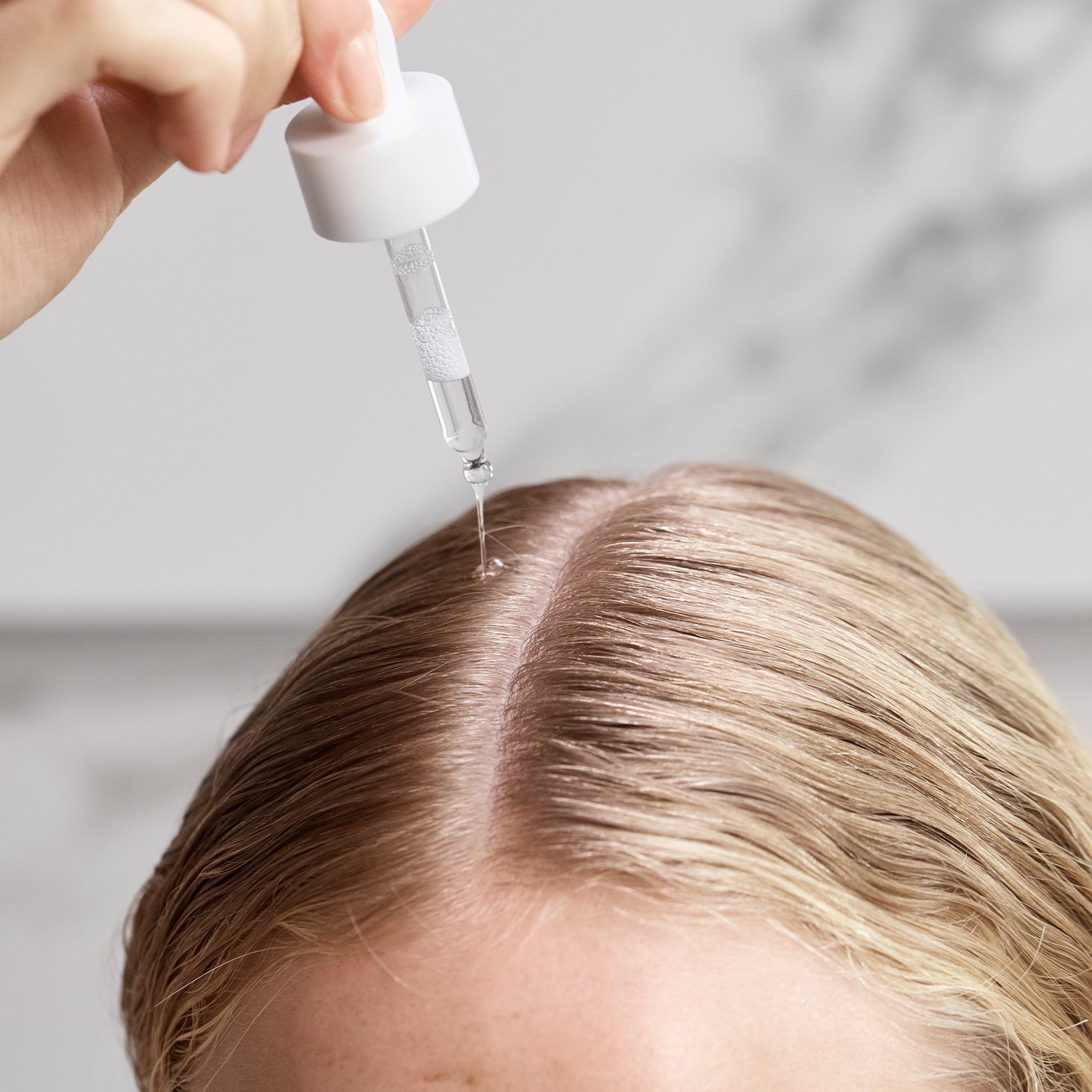 une personne versant une goutte de produit sur ses cheveux à l'aide d'un compte-gouttes