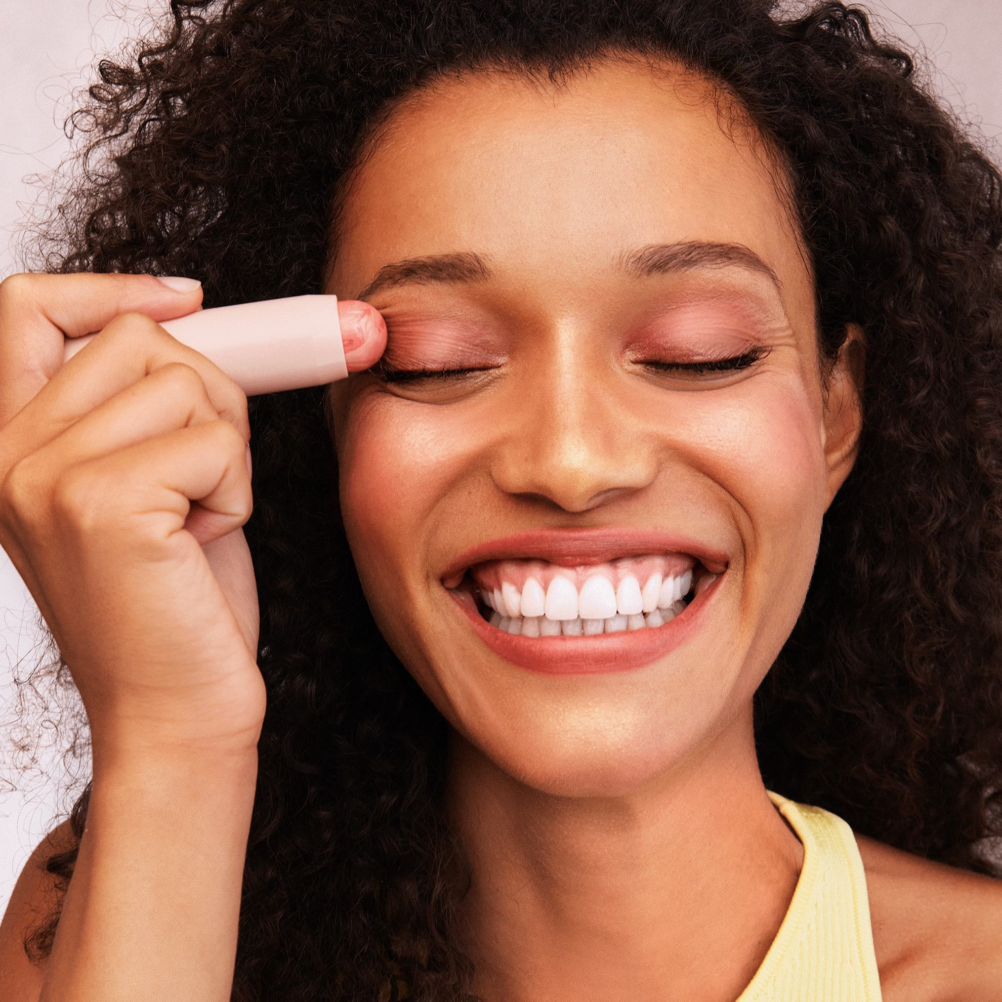 bir ayol jilmayib, ko'ziga lab bo'yog'i ushlab turadi