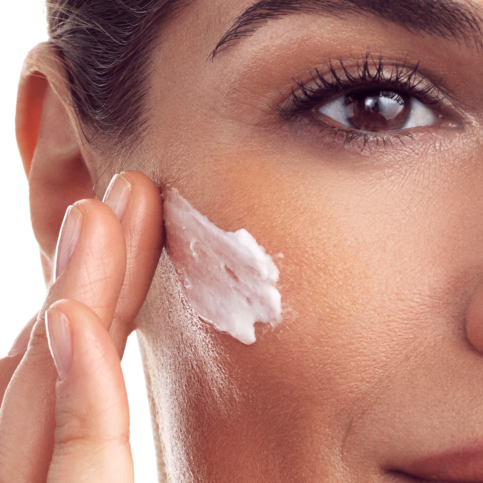 Primer plano de una mujer aplicándose crema en la cara.