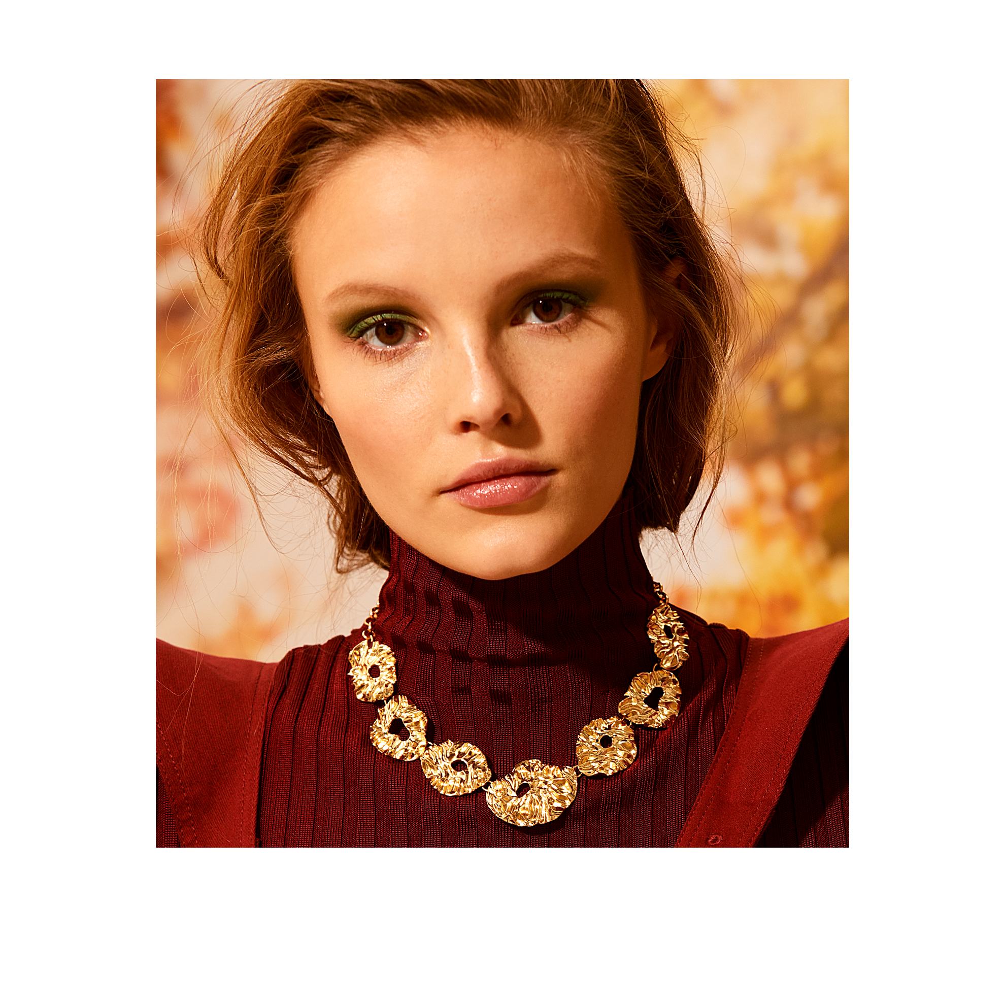 Una mujer con un jersey de cuello alto rojo y un collar dorado.