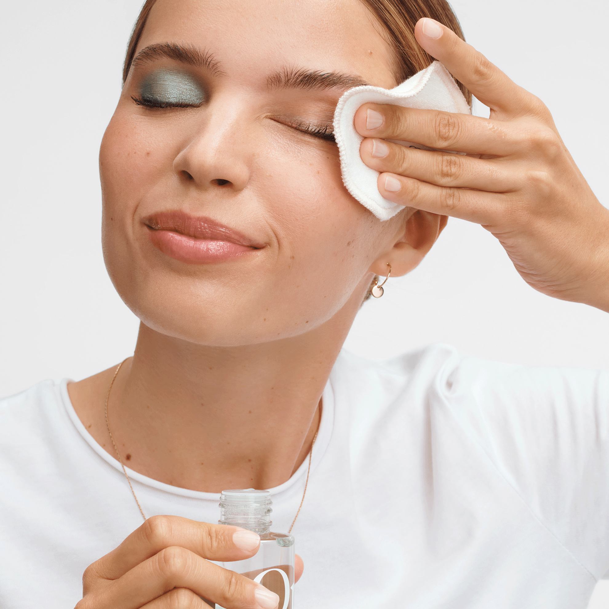 o femeie cu un disc de bumbac și demachiant pentru ochi