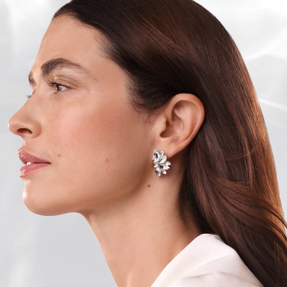 een vrouw met lang bruin haar, gekleed in een wit shirt en met diamanten oorbellen