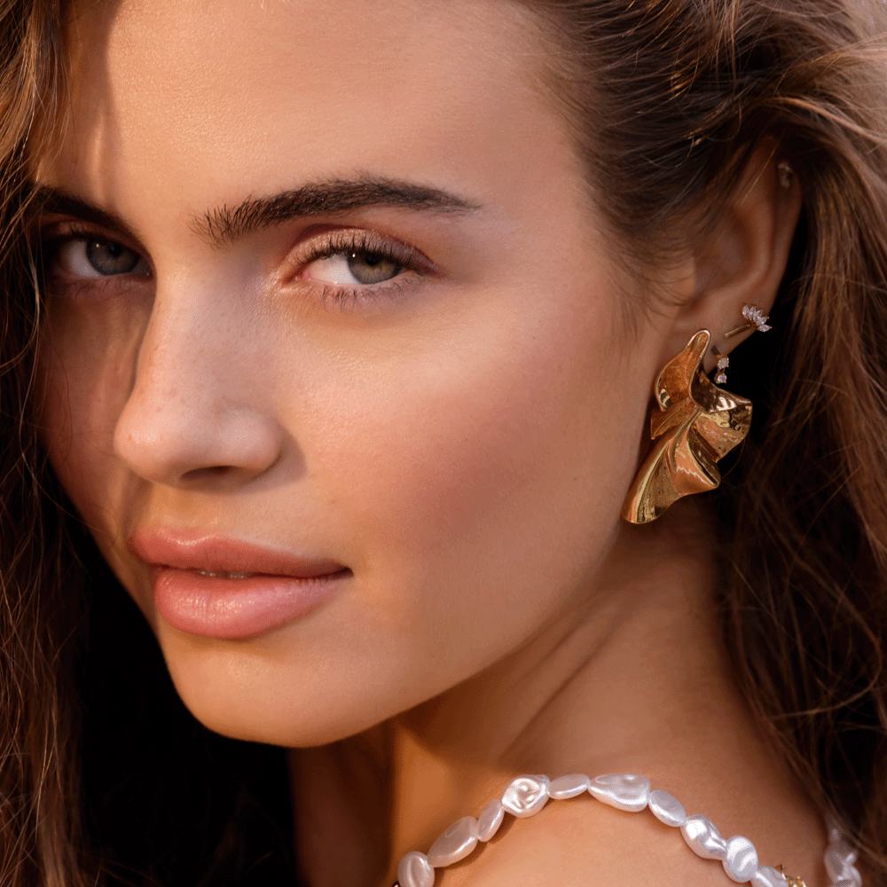 Una mujer con el pelo largo y castaño que lleva un pendiente de oro y un collar de perlas