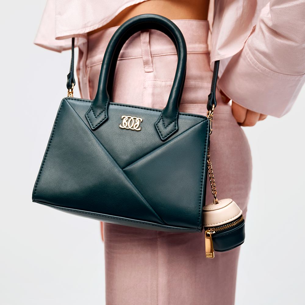 մի կին, որը կրում է վարդագույն շալվար և վարդագույն բաճկոն, որը սև քսակ է պահում