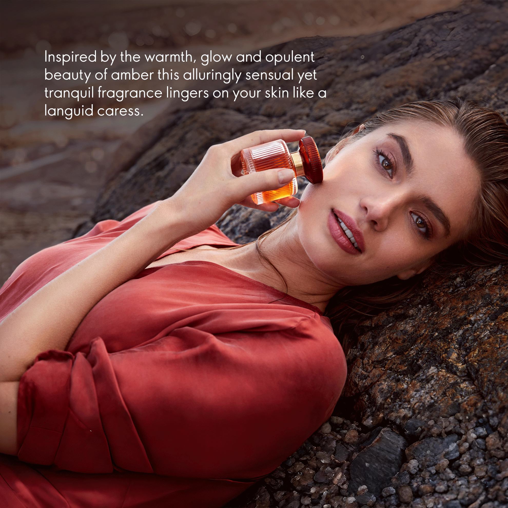a woman lying on a rock holding a bottle of perfume