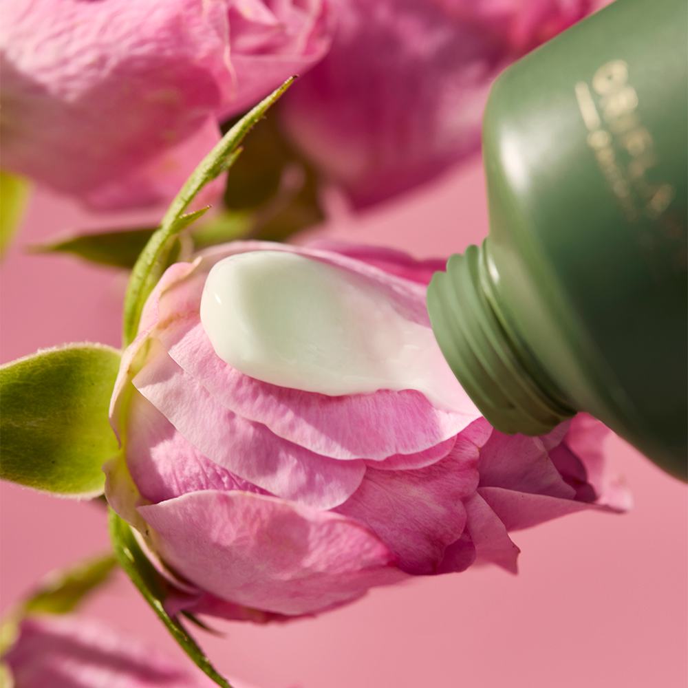 Una botella verde con líquido blanco sobre una flor rosa.